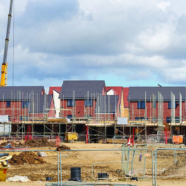 Development Finance Newly constructed houses with solar panels, construction site with cranes in the background.