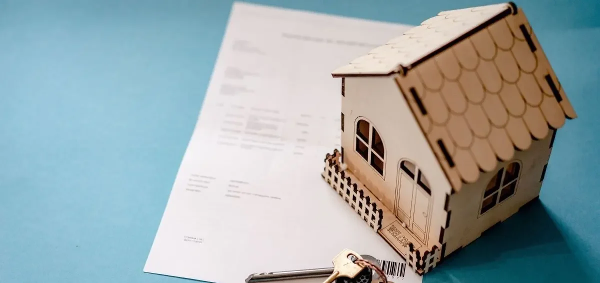 Bridging Loans Model wooden house on a blue surface next to a sheet of paper and a key.