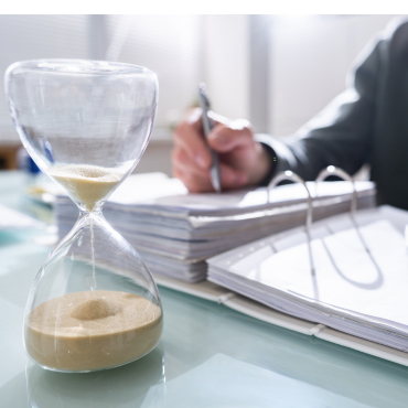 hourglass An hourglass on a desk with a person writing in a notebook.