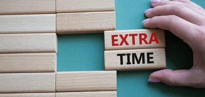 Exit Strategy Hand placing a wooden block marked "EXTRA" beside one marked "TIME" on a green surface.